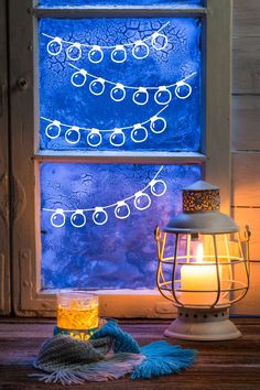 a lit candle sitting on top of a wooden table next to a window with blue frosting