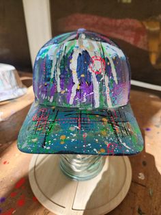 a baseball cap that is sitting on top of a wooden table with paint splatters all over it