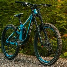 a blue mountain bike parked on top of a gravel road next to some green trees