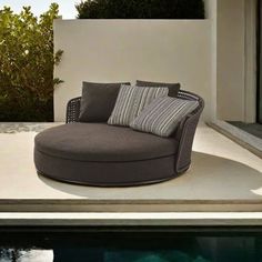 an outdoor lounge chair sitting next to a swimming pool with pillows on the back and sides