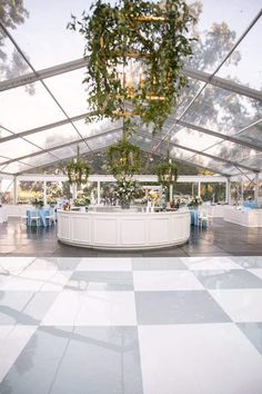 an outdoor reception area with tables and chairs under a large white tented structure, surrounded by greenery