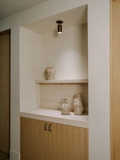 two vases are sitting on the counter in this room with white walls and wood cabinets