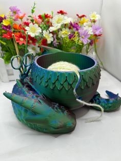 a green vase sitting on top of a white table next to colorful flowers and plants