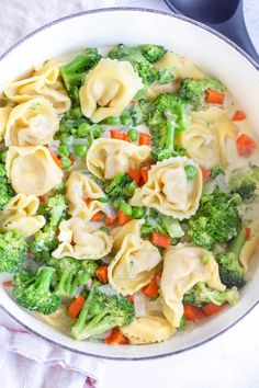 a pot filled with dumplings and broccoli on top of a white table