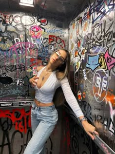 a woman leaning against a wall with graffiti on it and her arms behind her back