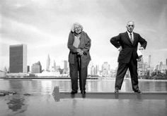 two people standing on a red object in front of a cityscape with skyscrapers