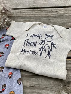 two baby onesuits are sitting next to each other on a wooden surface with the words i speak agent mandrake printed on them