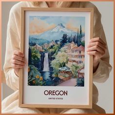 a woman holding up a framed poster with an image of a waterfall in the background