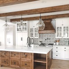 a large kitchen with white cabinets and wooden beams on the ceiling, along with marble counter tops