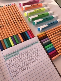 many different colored pencils are lined up next to each other on a table with writing paper