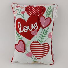 a red and white pillow with hearts that say love on the front, sitting on a table