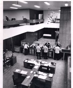 an old black and white photo of people in a room with desks, chairs and papers