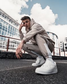 a man squatting on the ground with his hand near his face, in front of a building