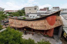 an unusual house with thatched roof in the middle of a cityscape, surrounded by trees and buildings