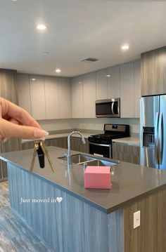 a hand holding a house key in front of a kitchen island with refrigerator and stove