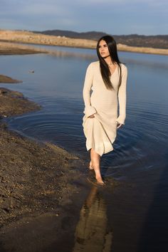 a woman is walking in the water with her hands on her hips and looking at the camera