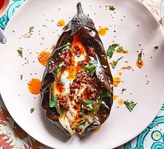 a white plate topped with an eggplant covered in sauce and other toppings