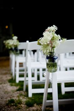 white chairs with flowers in them are lined up on the grass at an outdoor ceremony