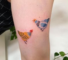 two colorful birds on the leg of a woman's legs, one is yellow and the other is blue