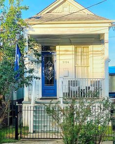 a white house with a blue door and fence in front of it on a sunny day