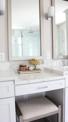 a white vanity with two mirrors and flowers on it's countertop in a bathroom