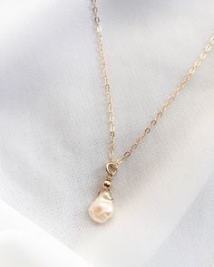 Classic and minimalist, a beautiful freshwater Keshi pearl hangs from our signature thin cable chain. With its organic shape and gorgeous luster, no two pearls are the same. Color ranges from cream and off-white to champagne. This dainty single pearl necklace is handcrafted in 14k Gold Filled or Sterling Silver. Wear alone or layer with your favorite everyday necklaces. Our model is wearing the 16" length necklace. Details: Single Freshwater Keshi Pearl (Approximately 7mm to 10mm In Size) Delica Pearl Minimalist Necklace, Perl Neckles Simple, Minimalist Gold Necklace With Pearl Drop, Minimalist Gold Pendant Pearl Necklace, Gold Feminine Pearl Pendant Necklace, Luxury Minimalist Pearl Pendant Necklace, Minimalist 14k Gold-filled Pearl Pendant Necklace, Minimal Choker, Gold Drop Necklace