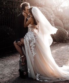 a bride and groom kissing in front of a fence with the sun shining down on them