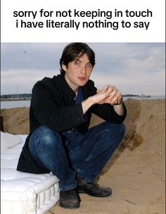 a man sitting on top of a mattress in the sand with his hand on his chin