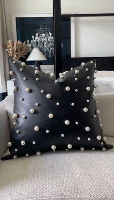 a black leather pillow with white pearls on it sitting on a couch next to a lamp