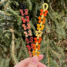 someone is holding two crocheted flowers in front of a pine tree with needles