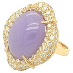 This exquisite convertible handcrafted 18k yellow gold ring features an oval shaped cabochon lavender jade. The center stone is enclosed in a unique design of 18K yellow gold with approximately 3.50 carats of round brilliant cut diamonds F color and VS clarity. The ring can be converted to a pendant. Just add it to a chain and wear it as a jade pendant necklace. It is a beautiful, unique, and versatile piece of jewelry. The ring top measures 1 inch by 1.25 inch. The ring is currently in size 8.5 and can be resized. Lavender Ring, Lavender Jade, Diamond Cocktail Rings, 18k Yellow Gold Ring, Domed Ring, Jade Pendant, Yellow Gold Ring, Round Brilliant Cut Diamond, Pink Sapphire