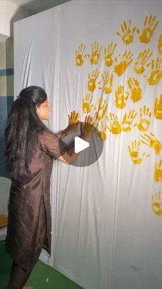 a woman standing in front of a wall with yellow hand prints on it