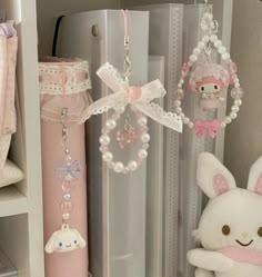 a white stuffed animal sitting next to a pink pen and keychain on a shelf