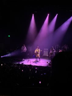 a group of people standing on top of a stage with purple lights in the dark