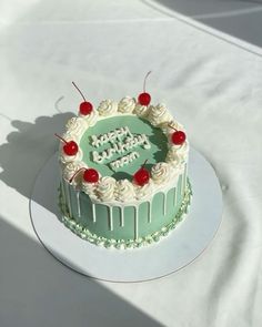 a birthday cake with white frosting and cherries on top, sitting on a table