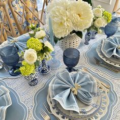 a table set with blue and white plates, silverware and flowers in vases