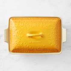 a yellow casserole dish on a marble countertop with the words le crueet written in french