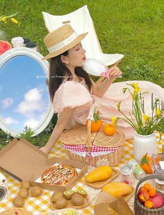 a woman in a pink dress and hat sitting on a picnic blanket with food around her