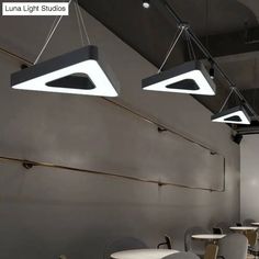 three suspended lights hang from the ceiling in a room with white tables and gray chairs