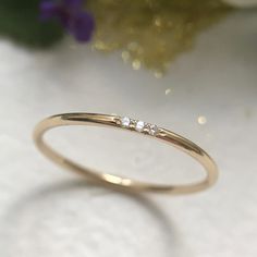 a yellow gold ring with three small diamonds on the side, sitting next to a purple flower