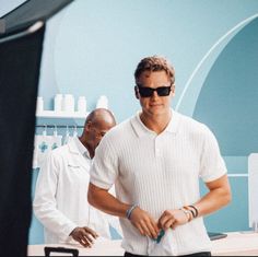 two men in white shirts and sunglasses are looking at something on the table with another man standing behind them