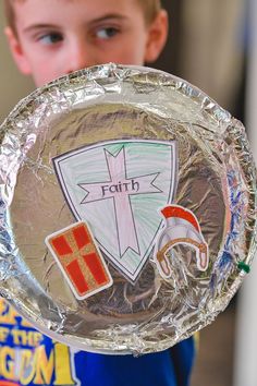 a young boy is holding up a paper plate with the word faith in front of him