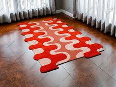 a red and white area rug on top of a hard wood floor next to windows