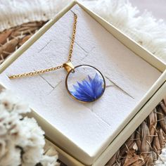 a necklace with a blue flower in it on a white box next to some flowers