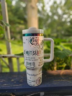 a coffee cup sitting on top of a wooden table in front of trees and bushes