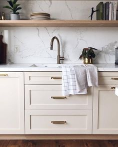 a kitchen with marble counter tops and white cabinets, gold pulls on the faucet