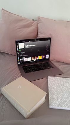 an open laptop computer sitting on top of a bed next to pillows and pillow cases