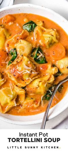 a white bowl filled with tortellini and spinach soup next to a spoon