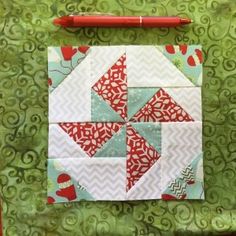 a piece of quilted material sitting on top of a green surface with a red pen next to it