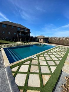 an empty swimming pool with artificial grass on the ground and in front of a house